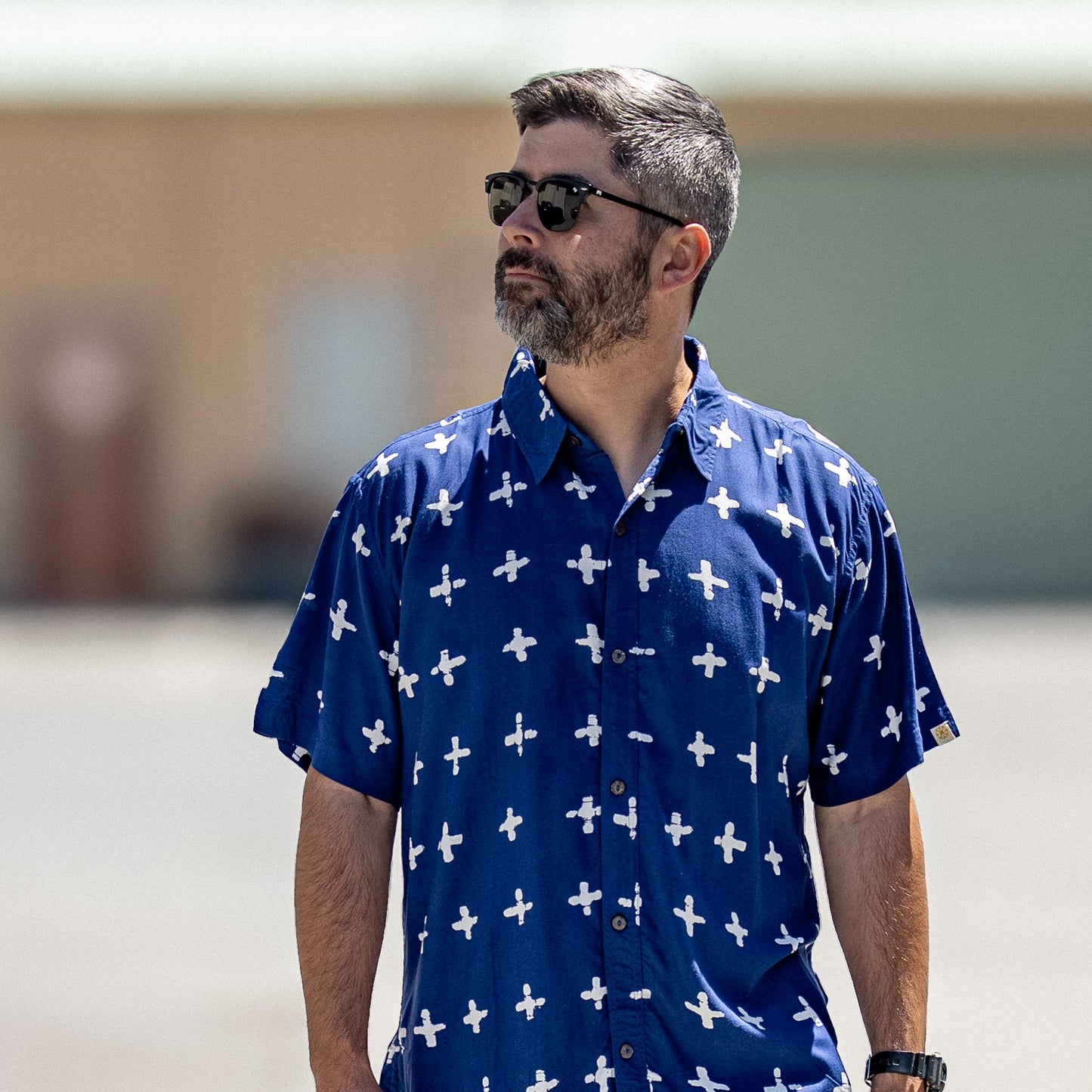 Man wearing a blue shirt with white patterns and black shorts outdoors.