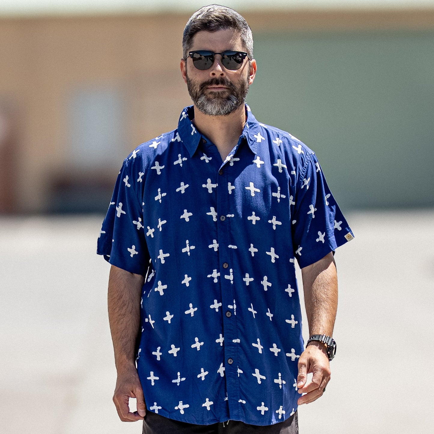 Man wearing a blue shirt with white patterns and black shorts outdoors.